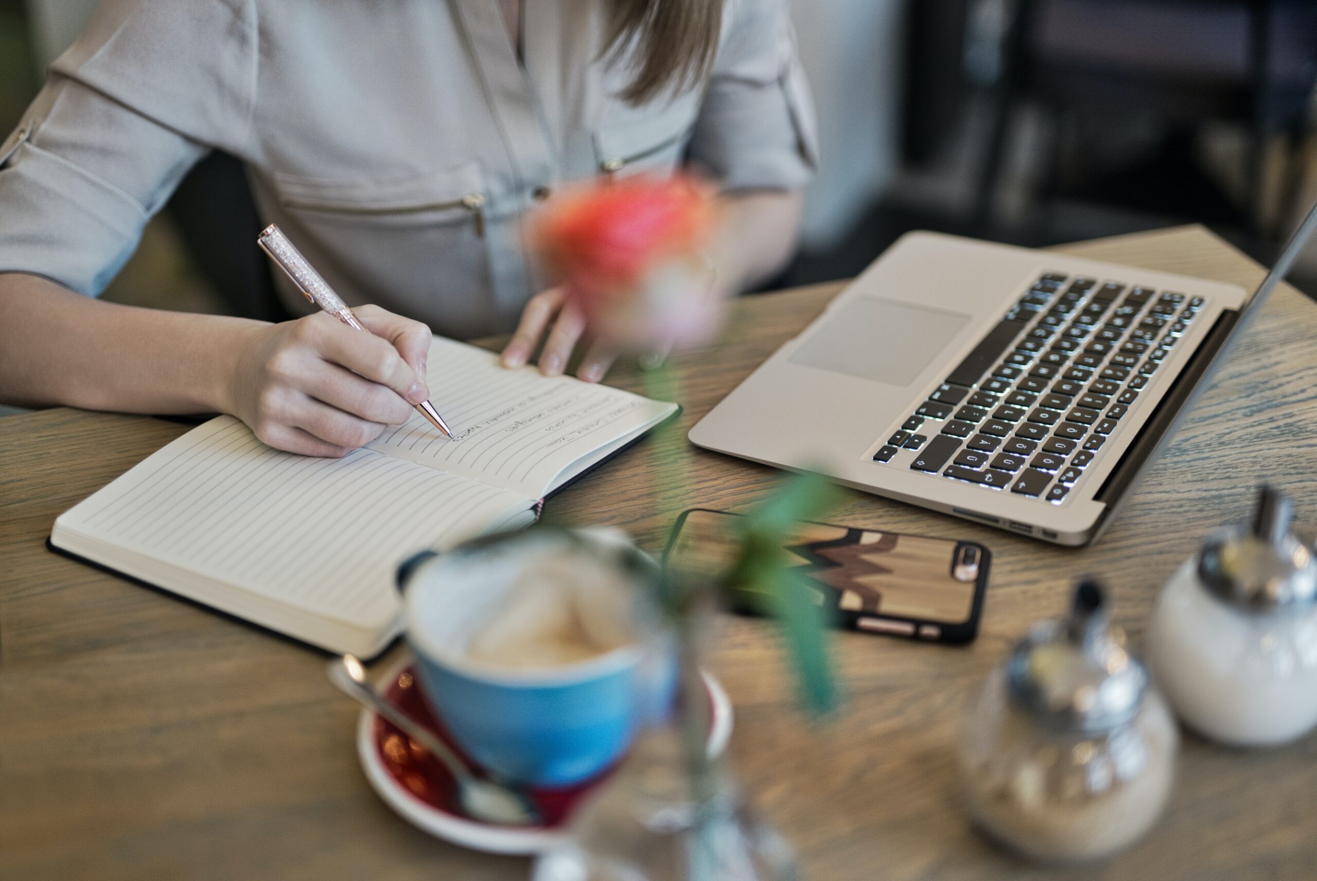 Kobieta robiąca notatki w zeszycie przed otwartym laptopem na biurku