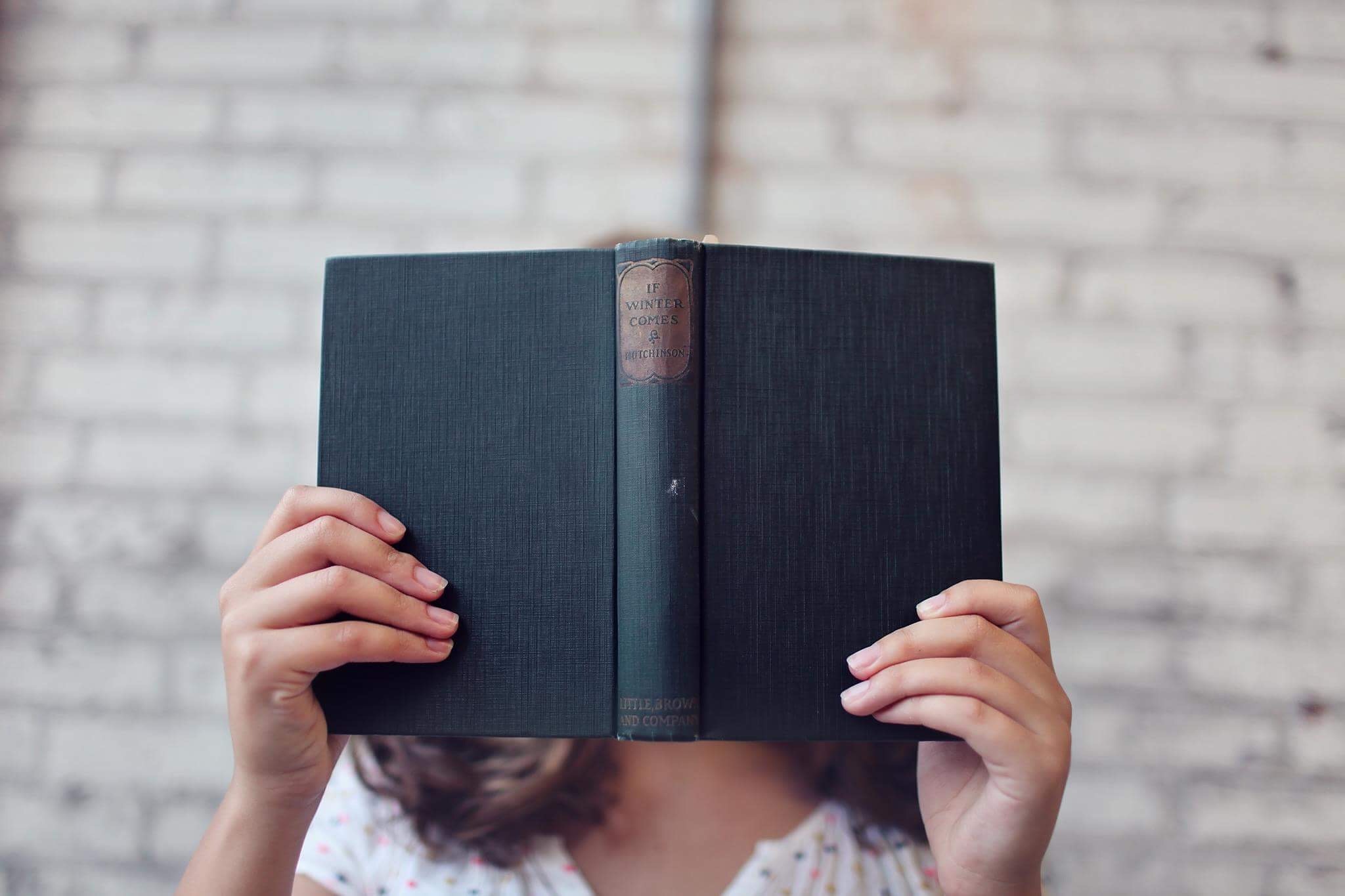 Kobieta trzymająca przed twarzą starą otwartą książkę w czarnej okładce