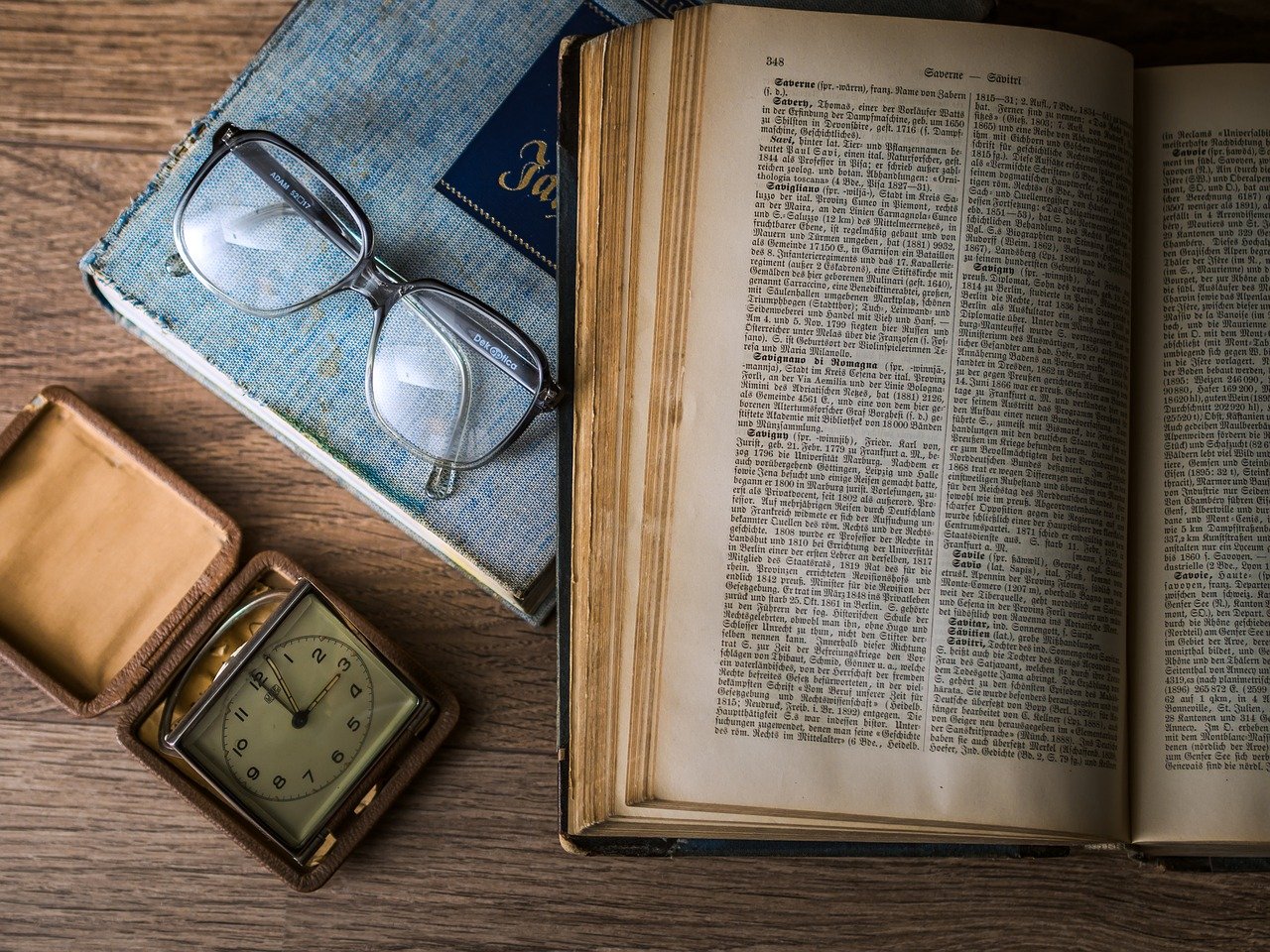 Stara otwarta księga, okulary i stary zegarek leżące na stole
